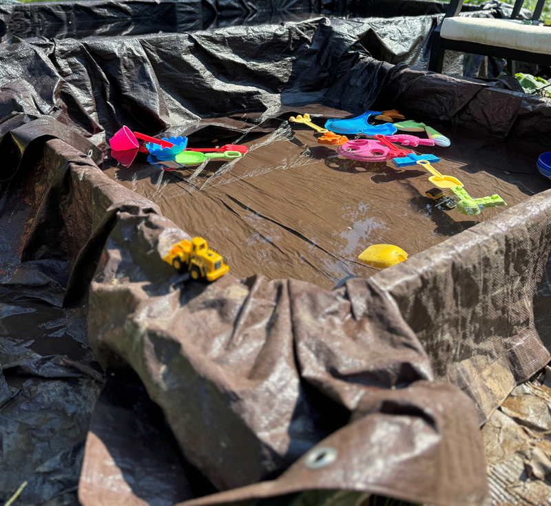 Hillbilly pool made from a tarp, with kids’ toys floating